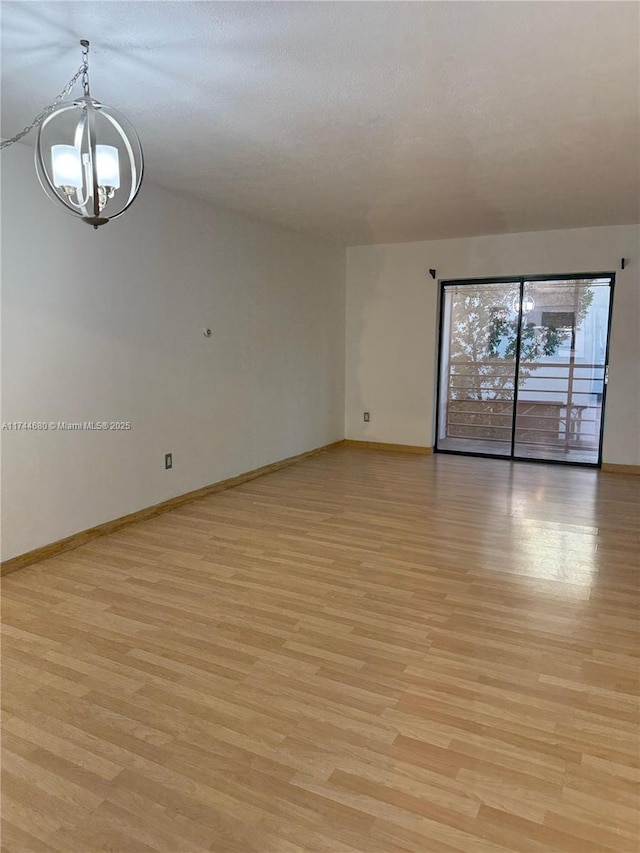 empty room with light wood finished floors, baseboards, and a notable chandelier