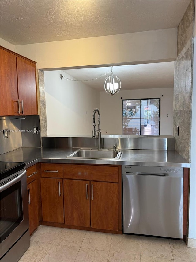 kitchen featuring decorative light fixtures, dark countertops, appliances with stainless steel finishes, brown cabinetry, and a sink