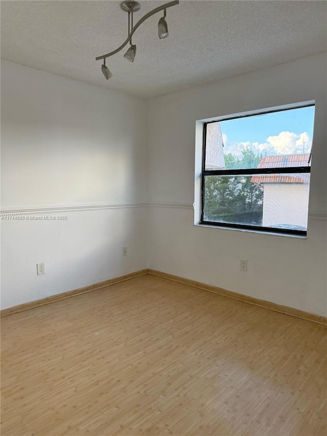 spare room with light wood-style floors, track lighting, baseboards, and a textured ceiling