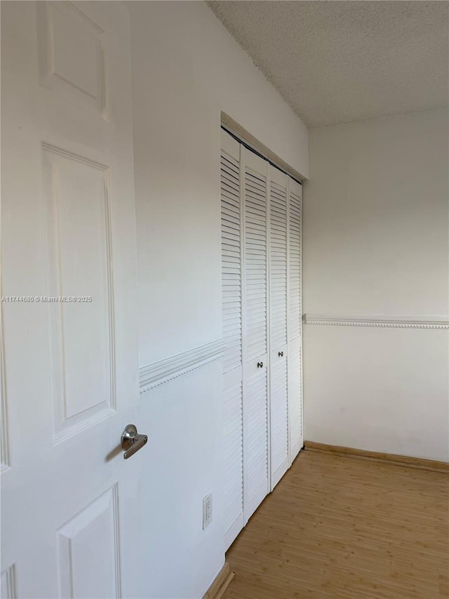 unfurnished bedroom featuring a textured ceiling, a closet, wood finished floors, and baseboards