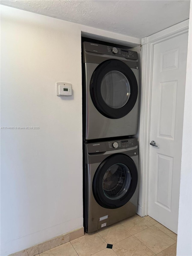 clothes washing area with stacked washer and dryer, light tile patterned floors, laundry area, baseboards, and a textured ceiling