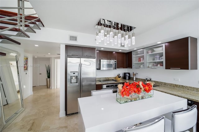 kitchen featuring decorative light fixtures, appliances with stainless steel finishes, glass insert cabinets, dark brown cabinetry, and a sink