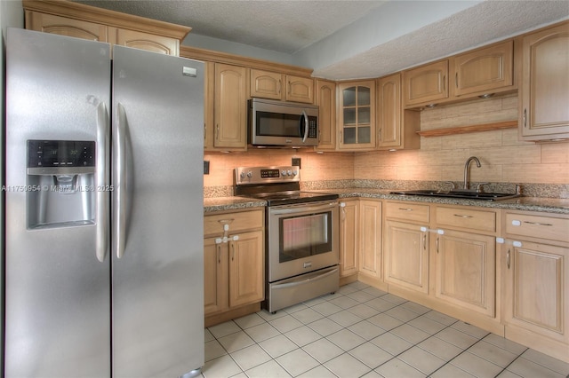 kitchen with tasteful backsplash, glass insert cabinets, stainless steel appliances, light brown cabinetry, and a sink