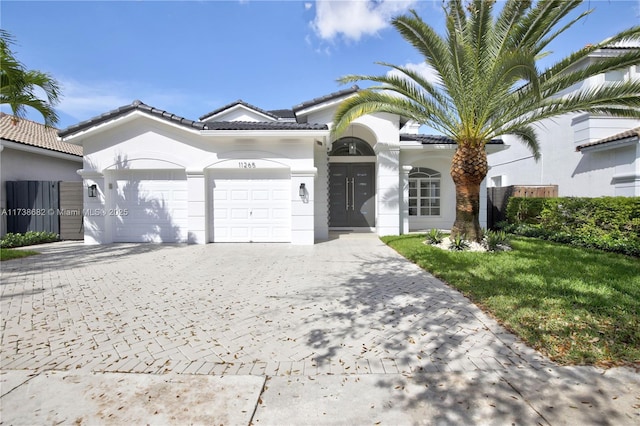 view of front facade with a garage, a tiled roof, decorative driveway, a front yard, and stucco siding