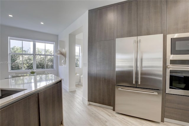 kitchen with light wood-style flooring, stainless steel appliances, dark brown cabinets, light countertops, and modern cabinets