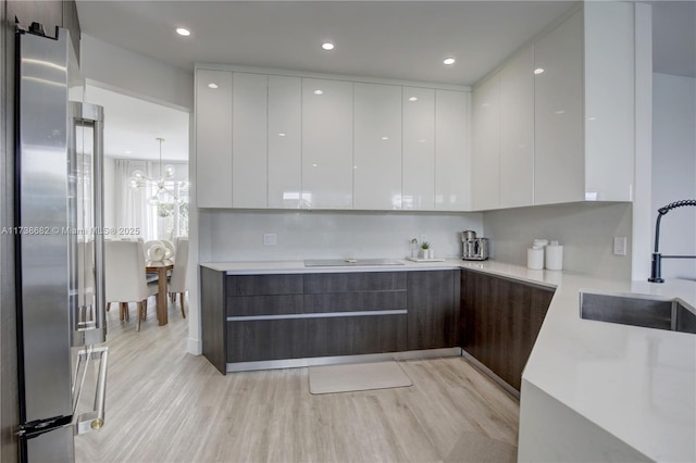 kitchen with high end refrigerator, white cabinets, modern cabinets, light countertops, and a sink