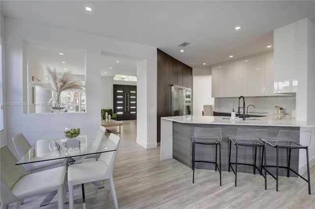 kitchen featuring light wood-style flooring, a peninsula, white cabinets, light countertops, and modern cabinets