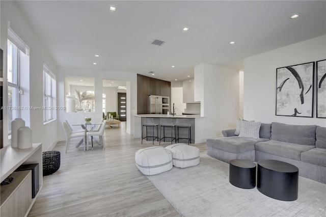 living room featuring baseboards, light wood-style flooring, visible vents, and recessed lighting