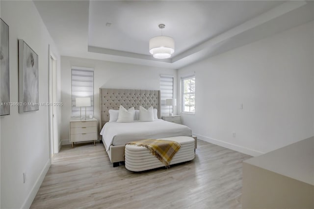 bedroom with a raised ceiling, light wood-style flooring, and baseboards