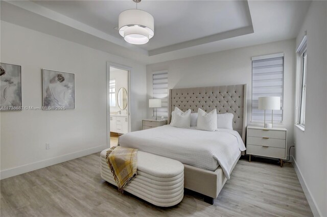 bedroom with light wood-style floors, a raised ceiling, and baseboards