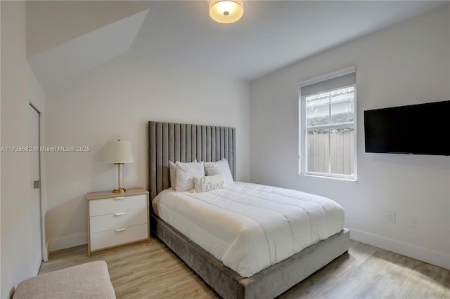 bedroom with light wood-style floors, vaulted ceiling, and baseboards