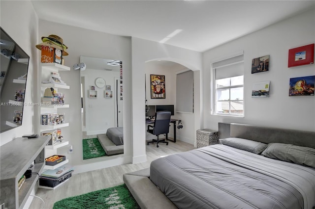 bedroom featuring arched walkways, light wood-style flooring, and baseboards