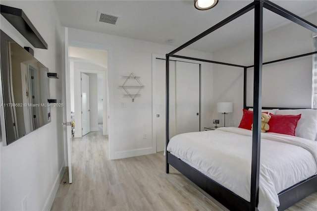 bedroom with light wood-style floors, baseboards, visible vents, and a closet