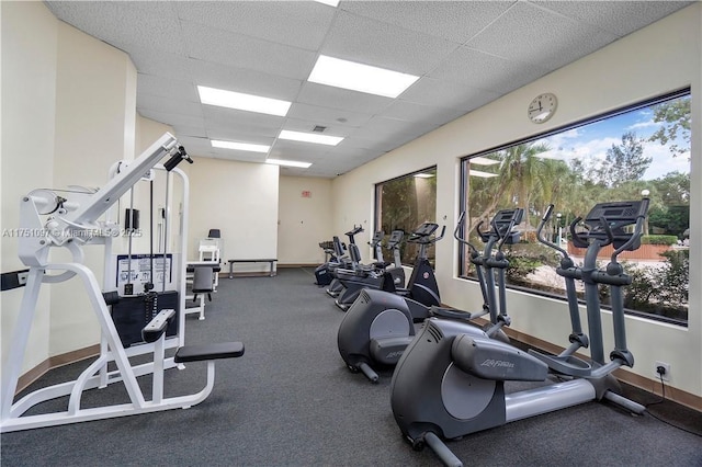 gym with a paneled ceiling and baseboards