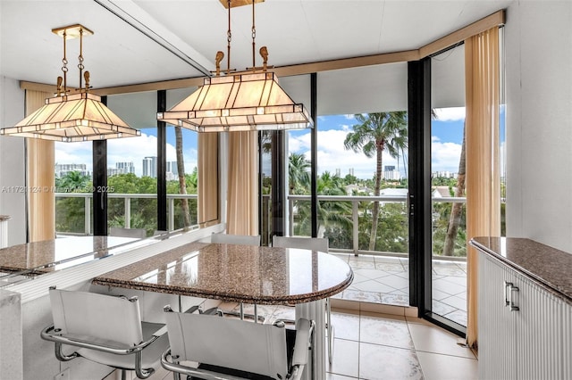 kitchen with light tile patterned floors, white cabinets, hanging light fixtures, expansive windows, and dark stone countertops