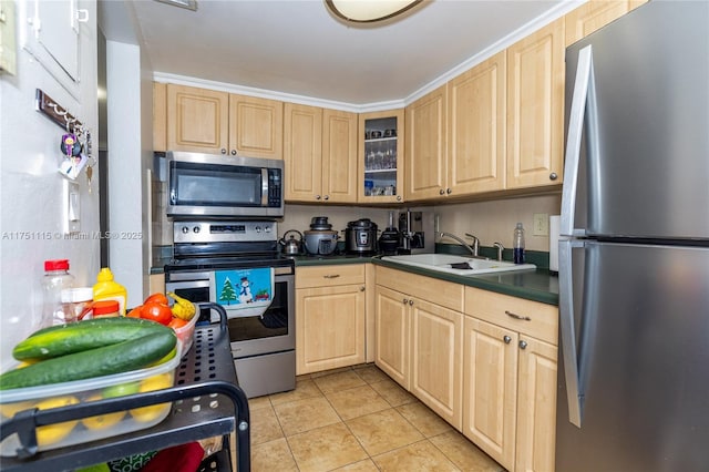 kitchen with dark countertops, glass insert cabinets, appliances with stainless steel finishes, a sink, and light tile patterned flooring