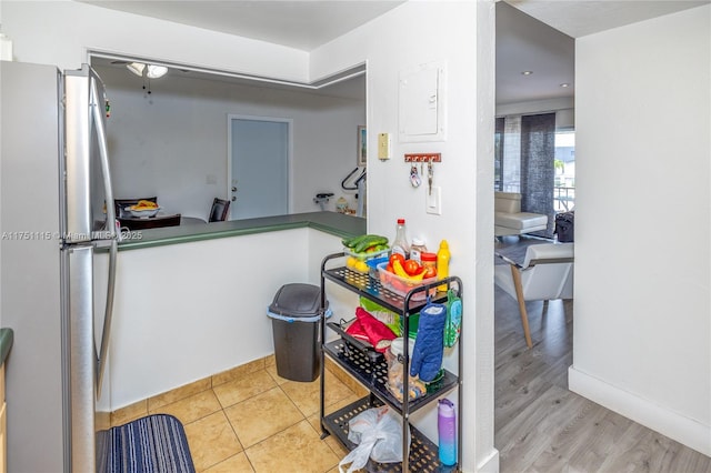 kitchen with light tile patterned floors, baseboards, freestanding refrigerator, and electric panel