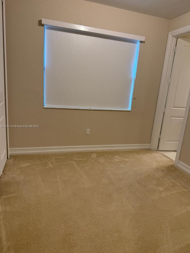 empty room featuring light carpet, a textured ceiling, and baseboards