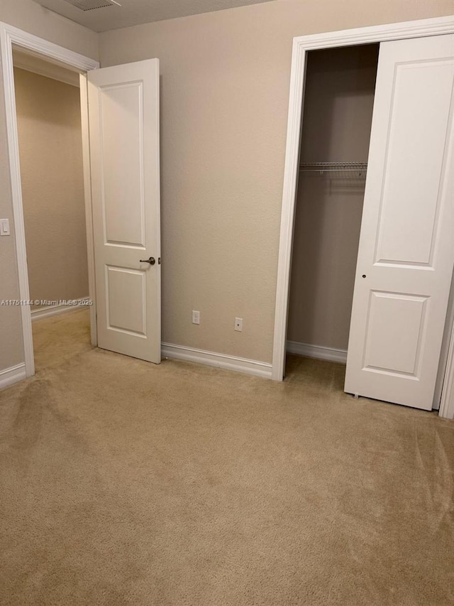 unfurnished bedroom with light carpet, a closet, and baseboards