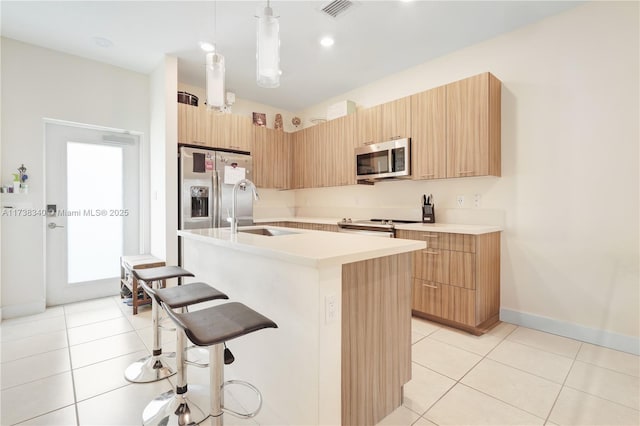 kitchen with a sink, hanging light fixtures, light countertops, appliances with stainless steel finishes, and an island with sink