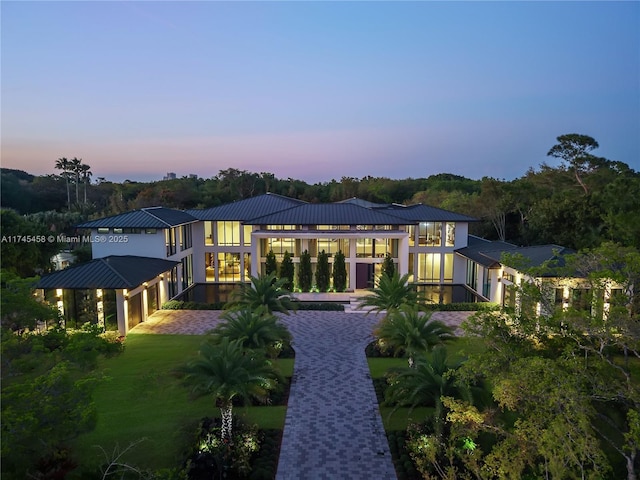 back of property at dusk featuring metal roof, a lawn, and a standing seam roof