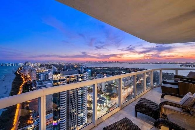 balcony at dusk with a water view and a view of city