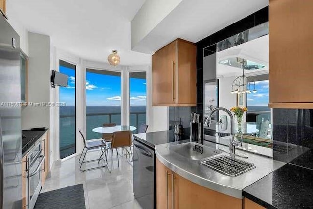 kitchen featuring a chandelier, a sink, appliances with stainless steel finishes, brown cabinetry, and dark countertops