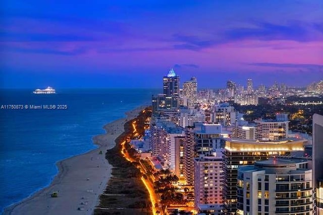 aerial view at dusk featuring a view of city, a water view, and a beach view