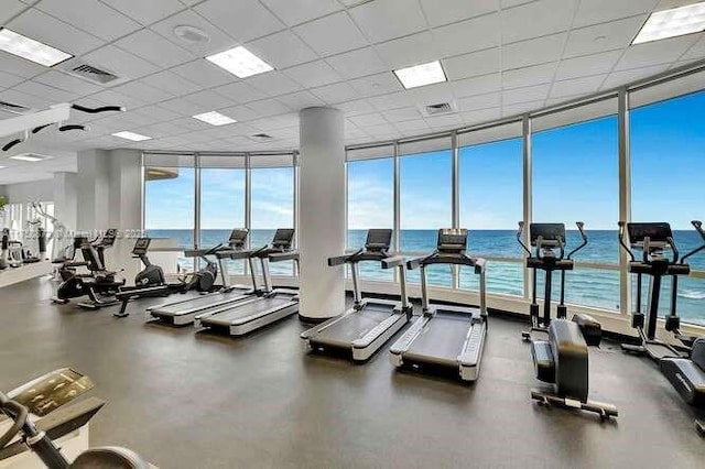 gym with expansive windows, a water view, a paneled ceiling, and visible vents