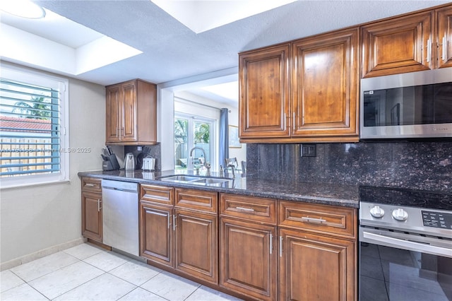 kitchen featuring brown cabinets, light tile patterned floors, stainless steel appliances, tasteful backsplash, and a sink