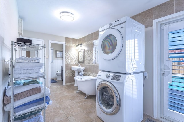 laundry room with laundry area, light tile patterned floors, a wealth of natural light, stacked washer / drying machine, and tile walls