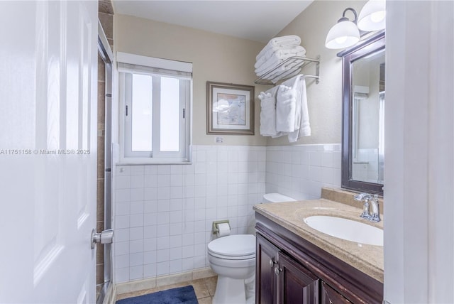 bathroom featuring toilet, a wainscoted wall, vanity, tile walls, and tile patterned floors