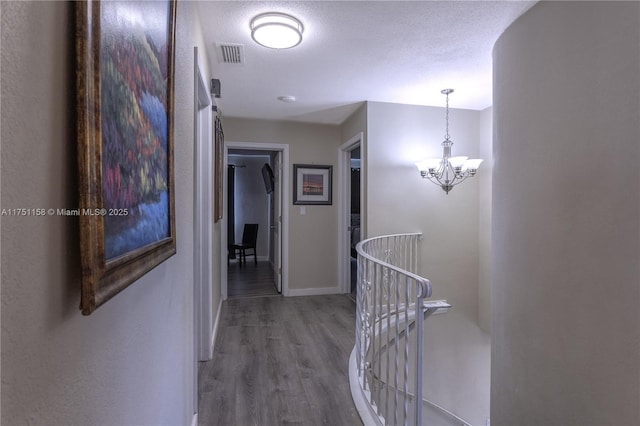 hall featuring a textured ceiling, wood finished floors, visible vents, and baseboards