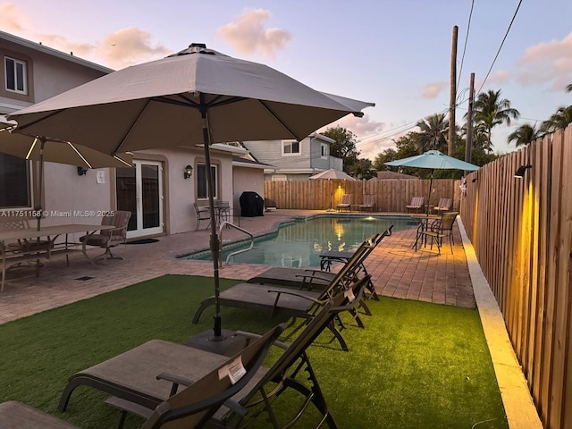 pool at dusk with a patio, a fenced backyard, a grill, a lawn, and a fenced in pool