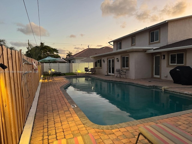 pool at dusk with area for grilling, a patio area, a fenced backyard, and a fenced in pool