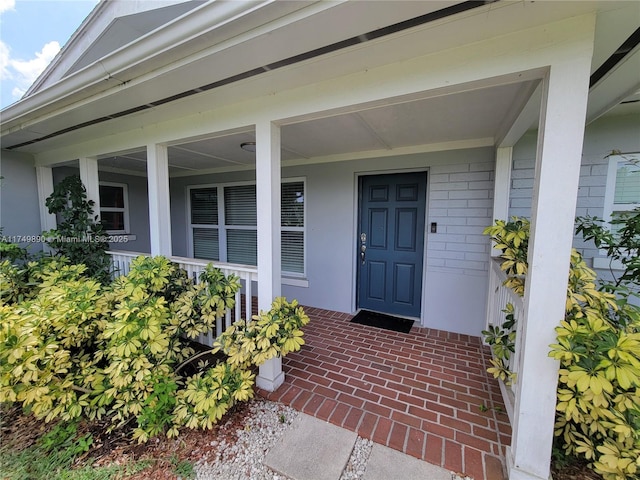 view of exterior entry with a porch and brick siding