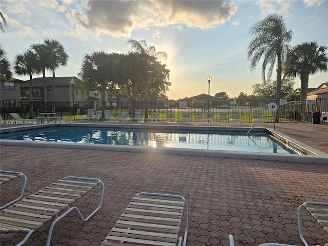 pool at dusk featuring a patio area, fence, and a community pool