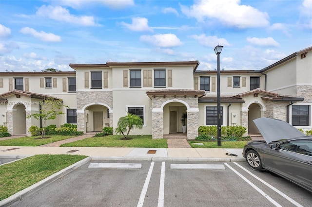 view of property featuring uncovered parking, stone siding, and stucco siding