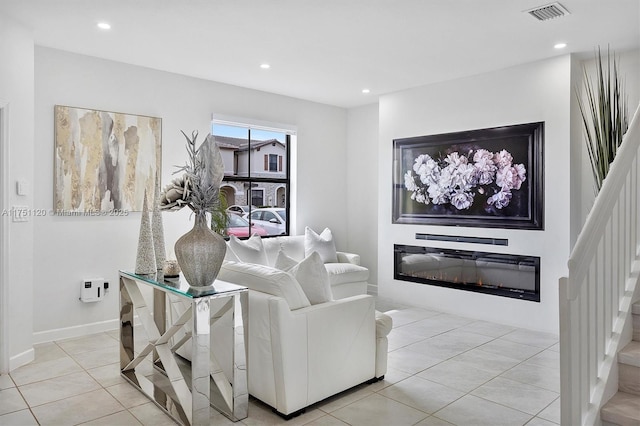 living room featuring light tile patterned floors, visible vents, a glass covered fireplace, stairway, and recessed lighting