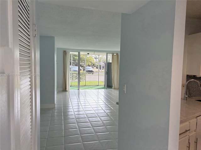 interior space with a textured ceiling, tile patterned flooring, a sink, and baseboards