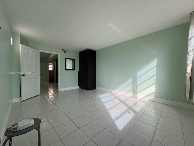 empty room with light tile patterned floors, baseboards, visible vents, and a textured ceiling