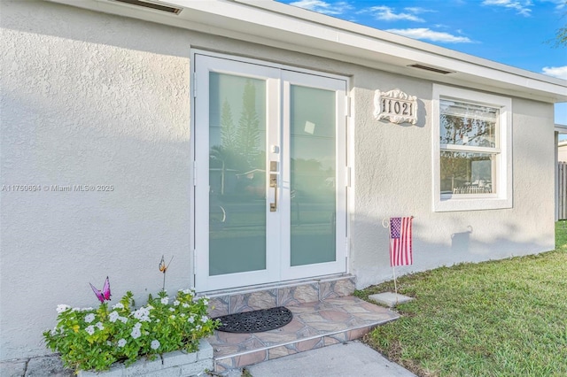 property entrance featuring stucco siding, a yard, and french doors