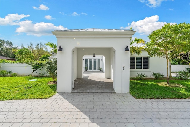 exterior space with french doors, stucco siding, a lawn, a standing seam roof, and metal roof