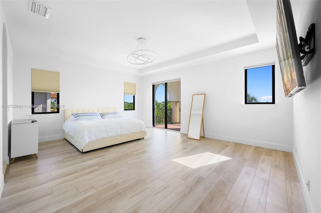 bedroom featuring light wood finished floors, visible vents, and a raised ceiling