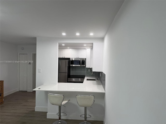 kitchen featuring stainless steel microwave, white cabinets, a peninsula, a kitchen bar, and fridge