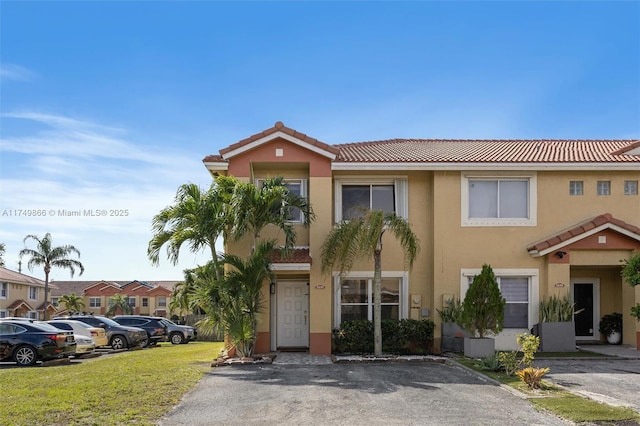 multi unit property with a tile roof, a residential view, uncovered parking, a front lawn, and stucco siding