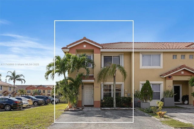 view of property with uncovered parking, a tile roof, a front lawn, and stucco siding