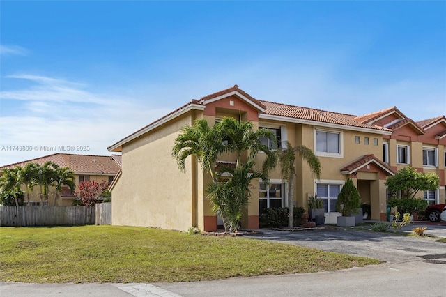 view of front of home with a tile roof, a front yard, fence, and stucco siding