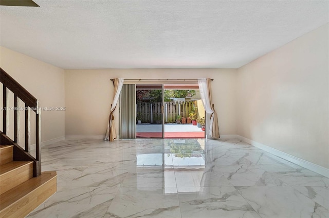 spare room with marble finish floor, baseboards, stairway, and a textured ceiling