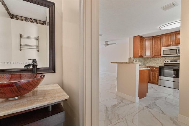 kitchen with marble finish floor, light countertops, appliances with stainless steel finishes, brown cabinetry, and a sink